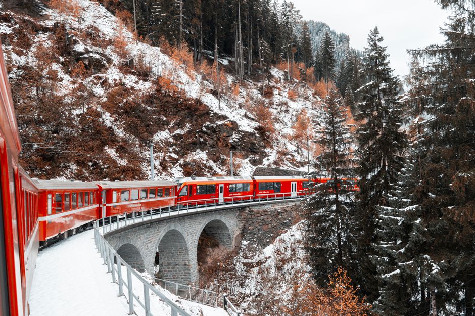 Red Swiss train winding through lush green mountains, symbolizing efficient travel in Switzerland