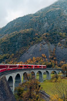 Red train traversing a scenic arch bridge in the Swiss Alps during autumn.