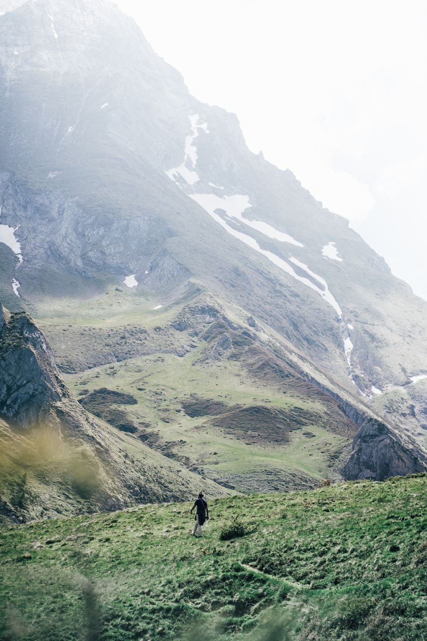 A lone hiker explores a misty mountain valley, surrounded by grass and towering peaks.