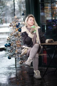 A woman enjoys a hot drink beside a decorated Christmas tree on a cold winter day.