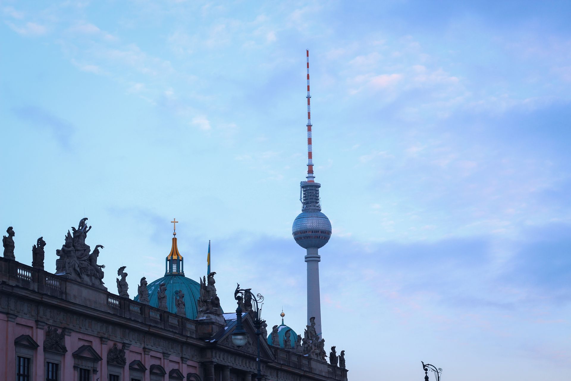 The iconic Berlin TV Tower and a historic architectural building under a blue evening sky.