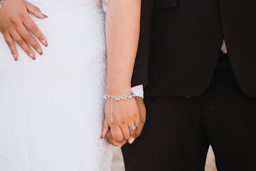 Close-up of a wedding couple holding hands, showcasing elegant attire and bridal jewelry.