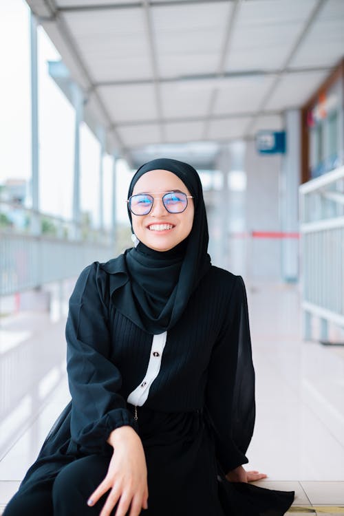 Smiling Woman Sitting on the Steps in a Headscarf and Eyeglasses
