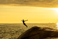 一名无所畏惧的男子在金色日落期间，从悬崖跳入大海象征着自由和冒险