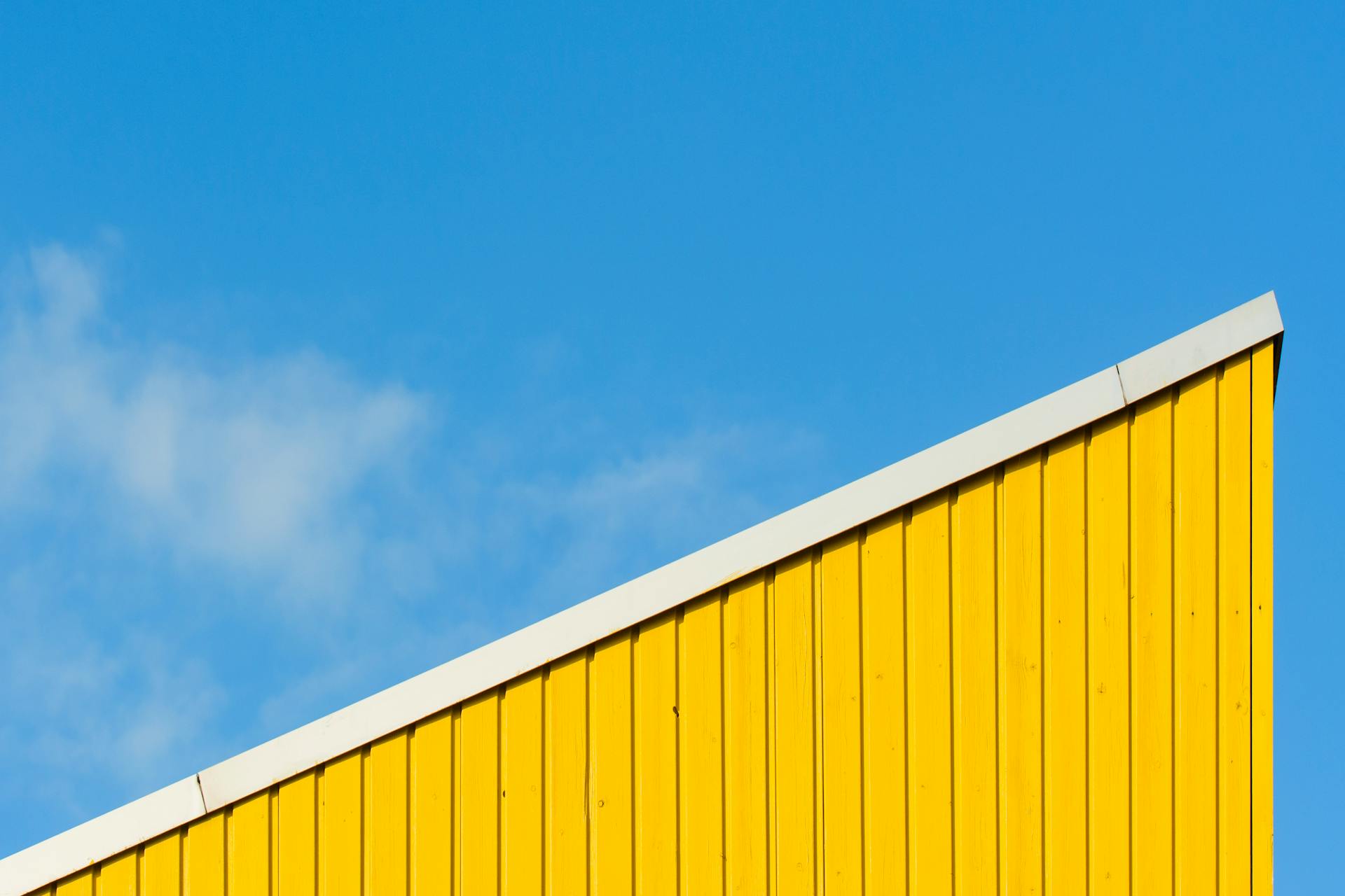 Minimalist architectural detail with a yellow roof against a blue sky.