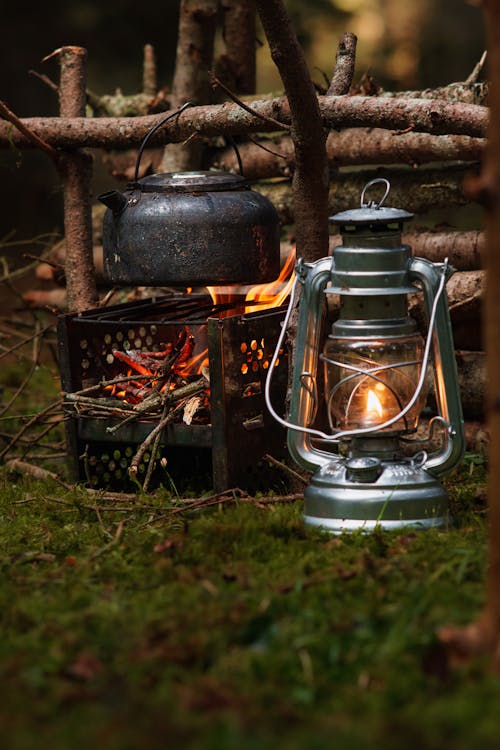 A Kettle Hanging over a Campfire and a Lantern Standing on the Ground 