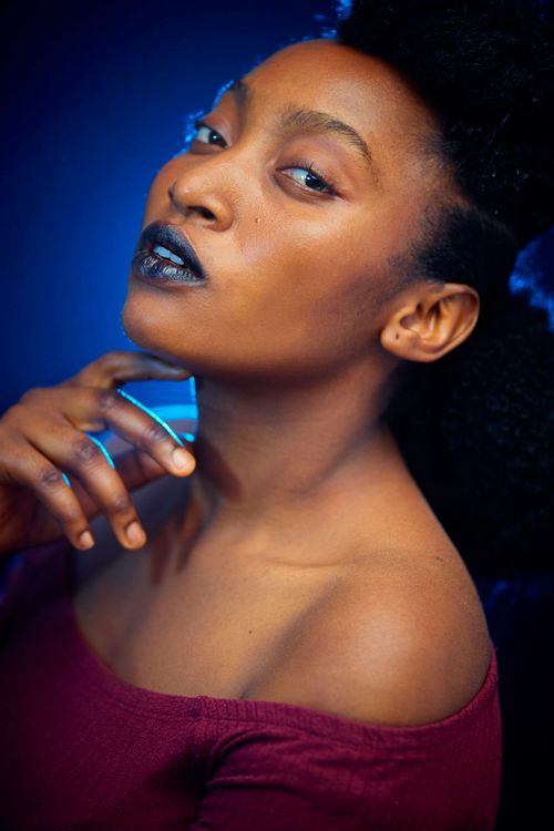 Free Portrait of a confident woman with blue background, hand on chin. Vibrant lighting and expressive pose. Stock Photo