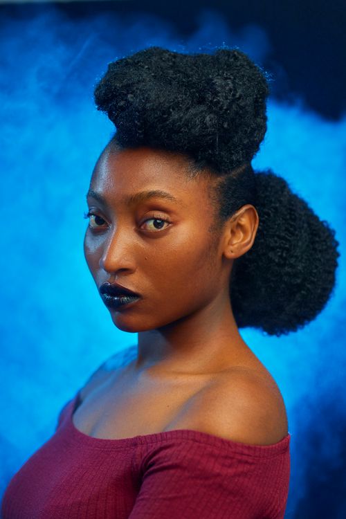 Free Vibrant studio portrait featuring a fashionable woman with an intricate hairstyle and striking attire. Stock Photo