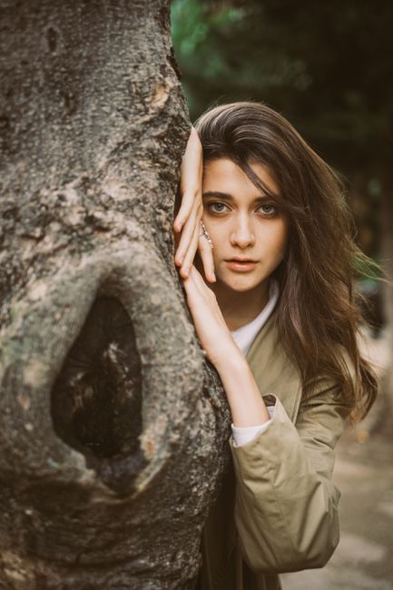 A striking portrait of a young brunette woman leaning against a tree in Lisbon, exuding elegance.