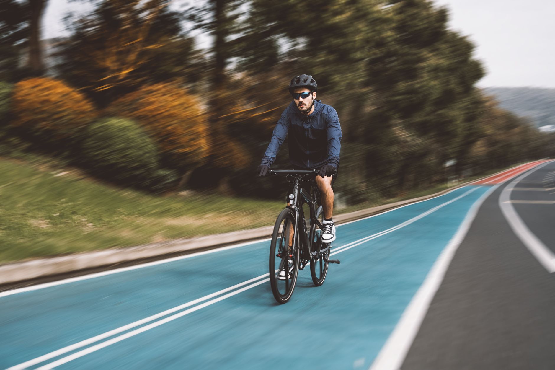 A man wearing sportswear cycles on a vibrant blue bike path surrounded by autumn scenery.