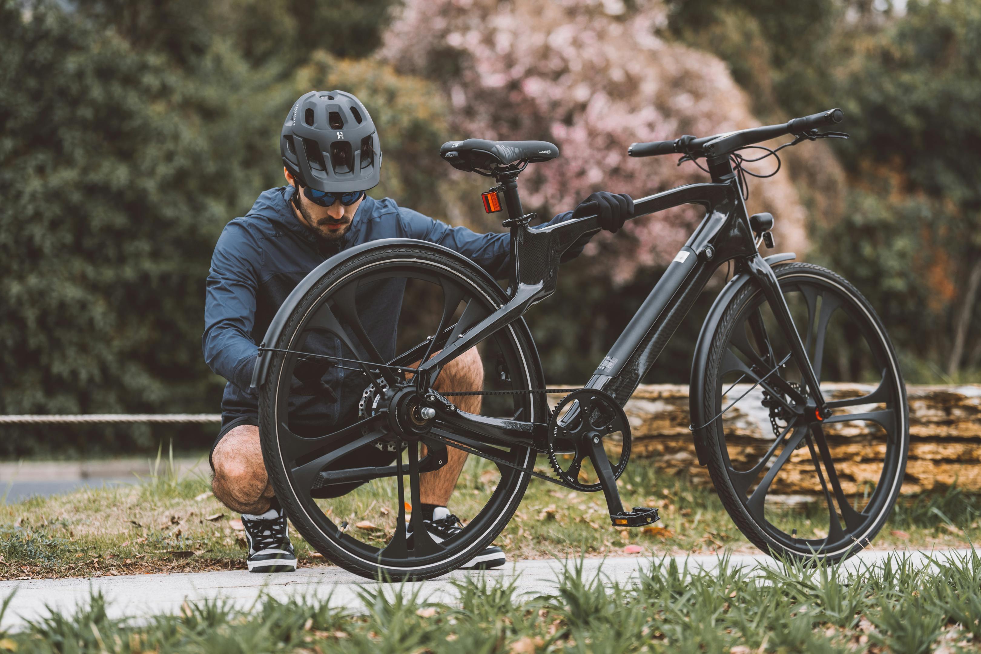 A cyclist adjusting his bike outdoors during spring in a natural setting, wearing a helmet.