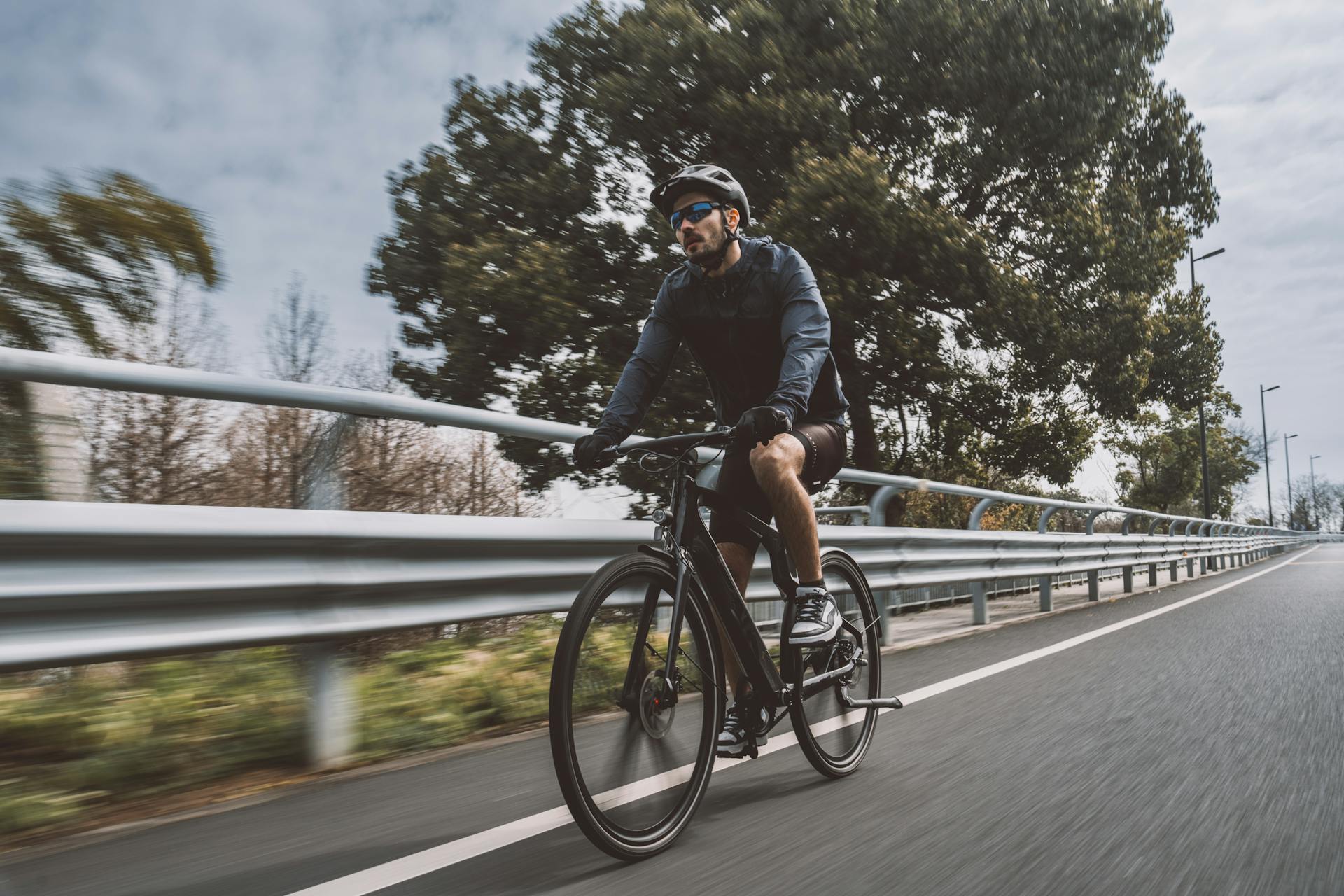 A cyclist rides a bicycle on an asphalt road surrounded by greenery, showcasing an active lifestyle.