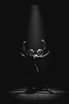 Two dancers perform gracefully in a spotlight, captured in black and white.