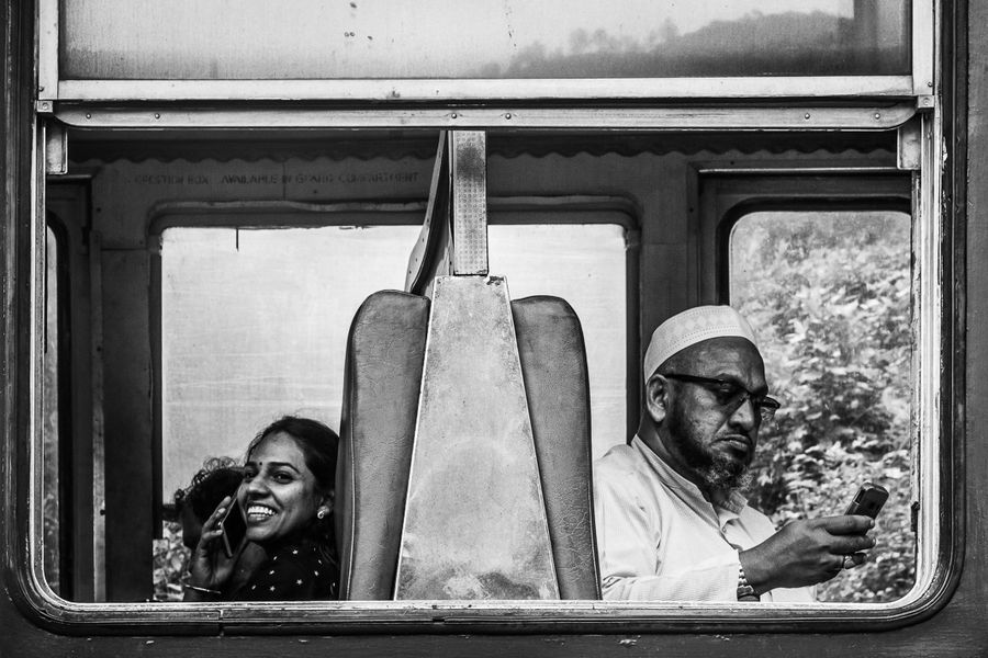 Black and white photo of two passengers in an Indian train, capturing a candid moment.