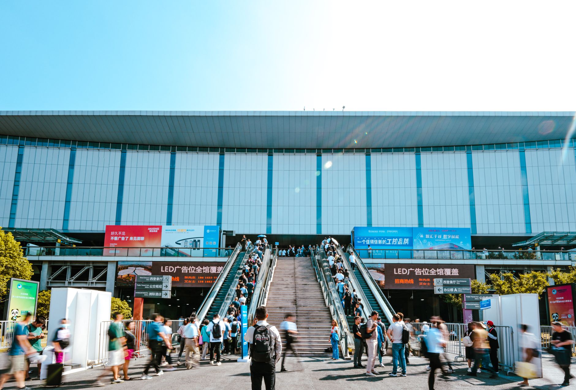 People entering Shanghai exhibition center via outdoor escalator during daytime.