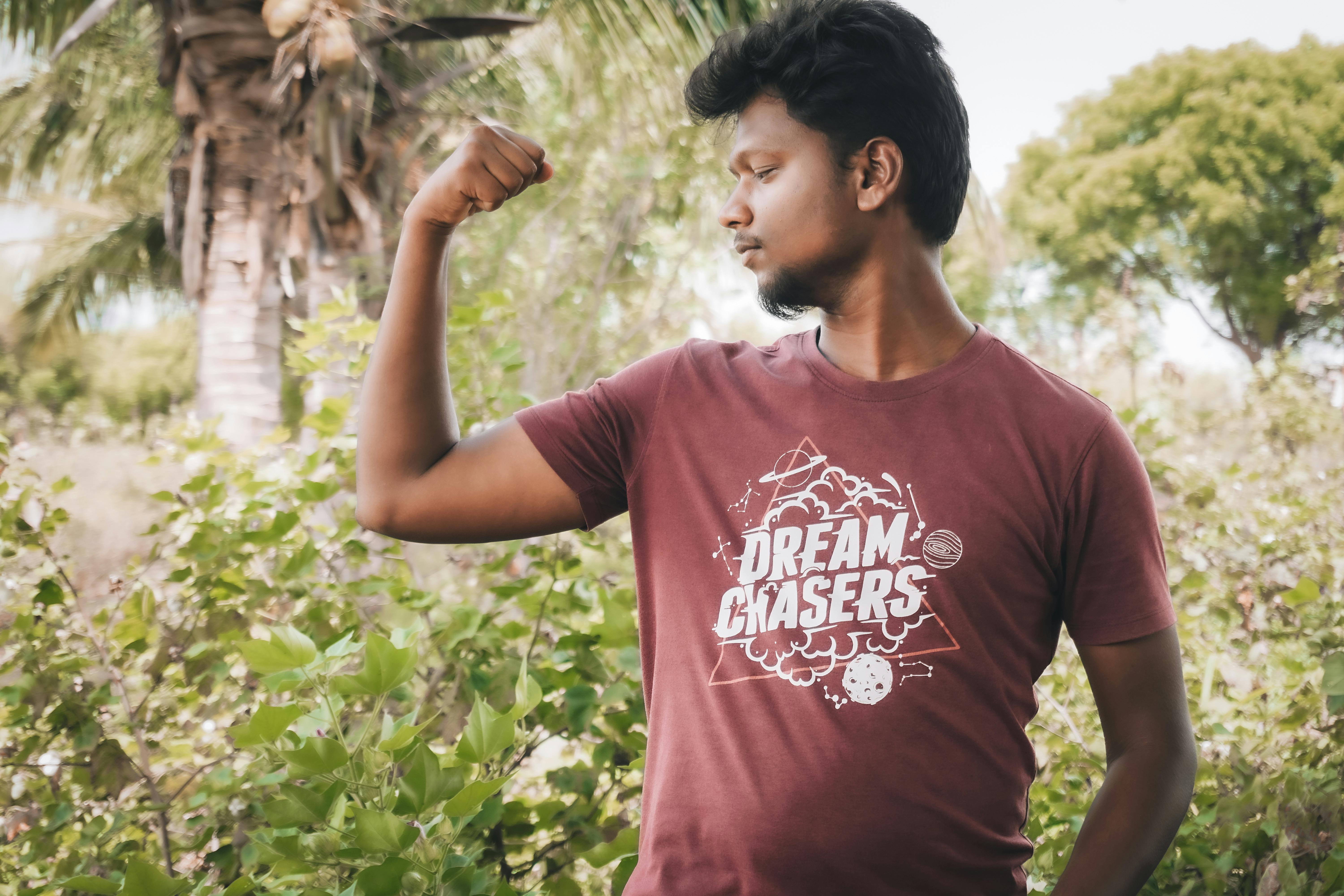 Young man flexing bicep outdoors in a summer garden setting.