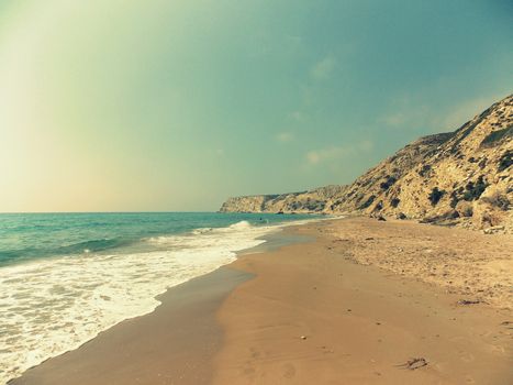 Peaceful view of a sandy beach with gentle waves and rocky cliffs under a sunny sky.