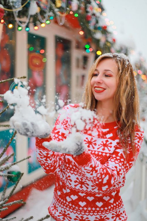 Free Smiling woman in red sweater enjoying snow with holiday lights background. Stock Photo