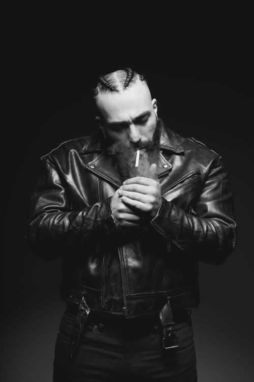 Free Intense black and white portrait of a man in a leather jacket lighting a cigarette. Stock Photo