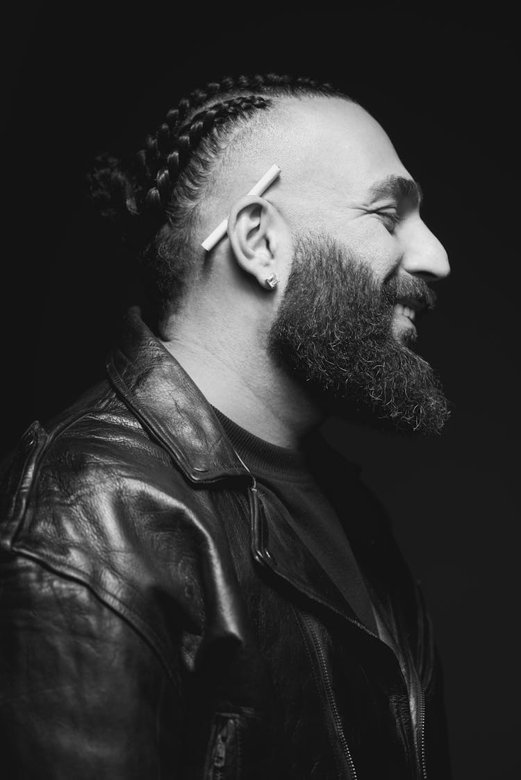 Smiling Bearded Man With Braided Hair And A Cigarette Behind His Ear In Profile