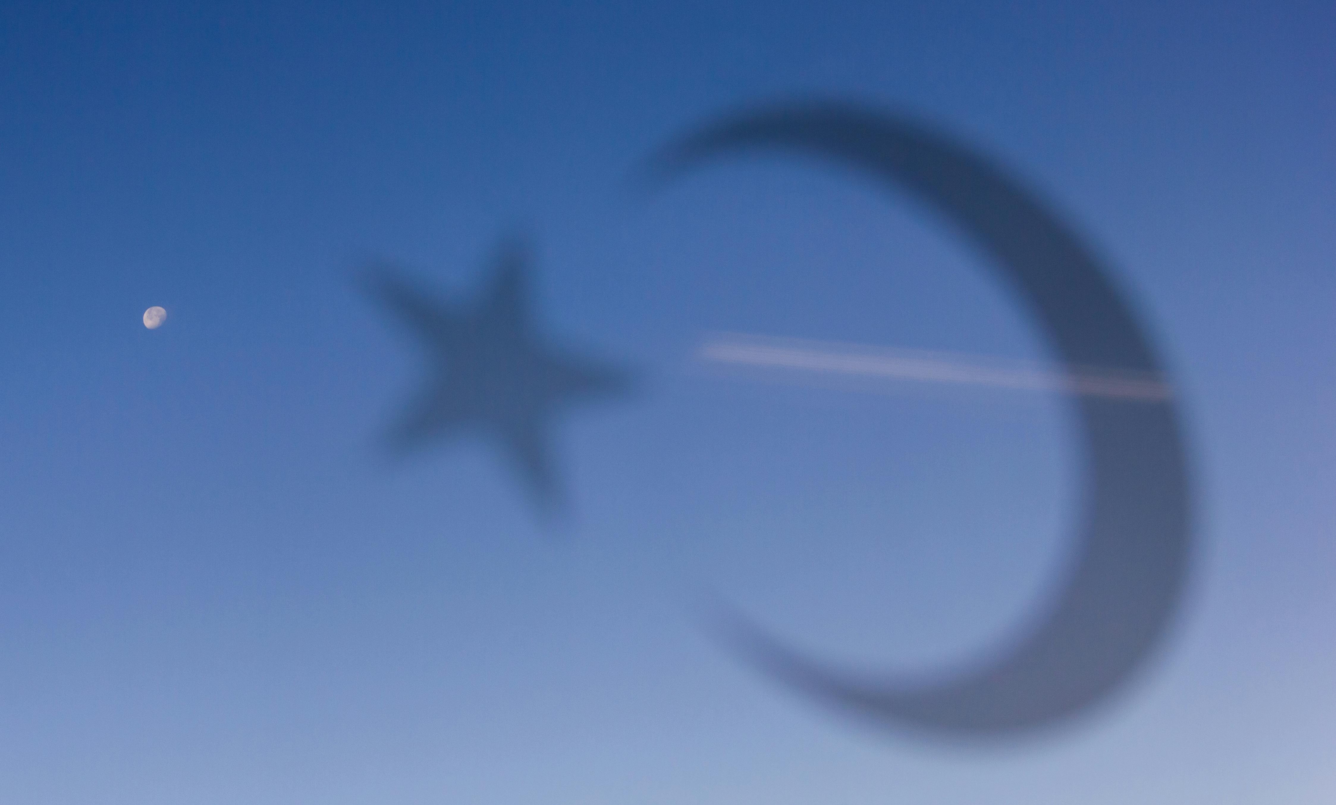 Crescent moon and star blurred in a blue sky with aircraft contrail.