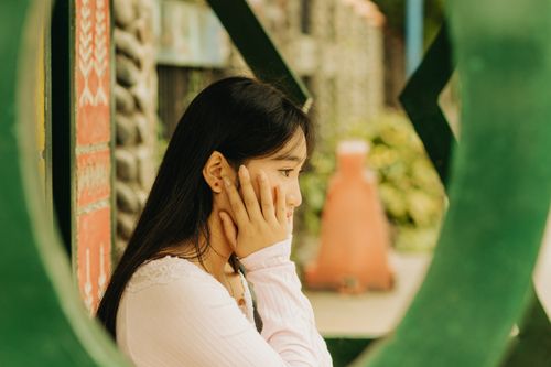 Free A young Asian woman in a contemplative pose outdoors, framed by urban features. Stock Photo