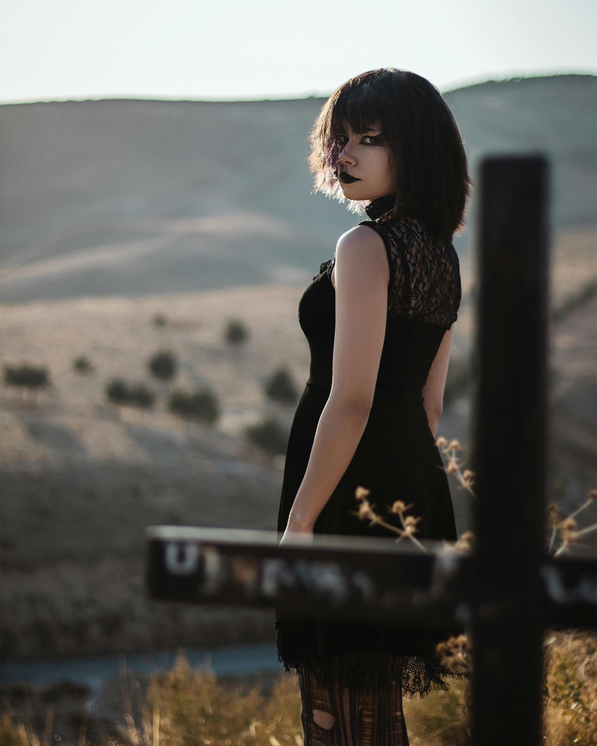 Gothic style portrait of a woman in a black dress looking over her shoulder in an open landscape.