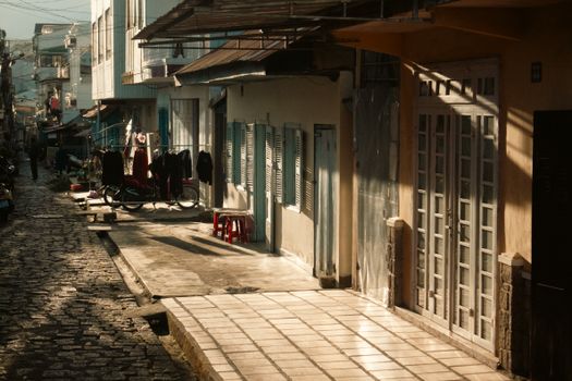A charming sunlit street in a village with rustic buildings and cobbled paths.
