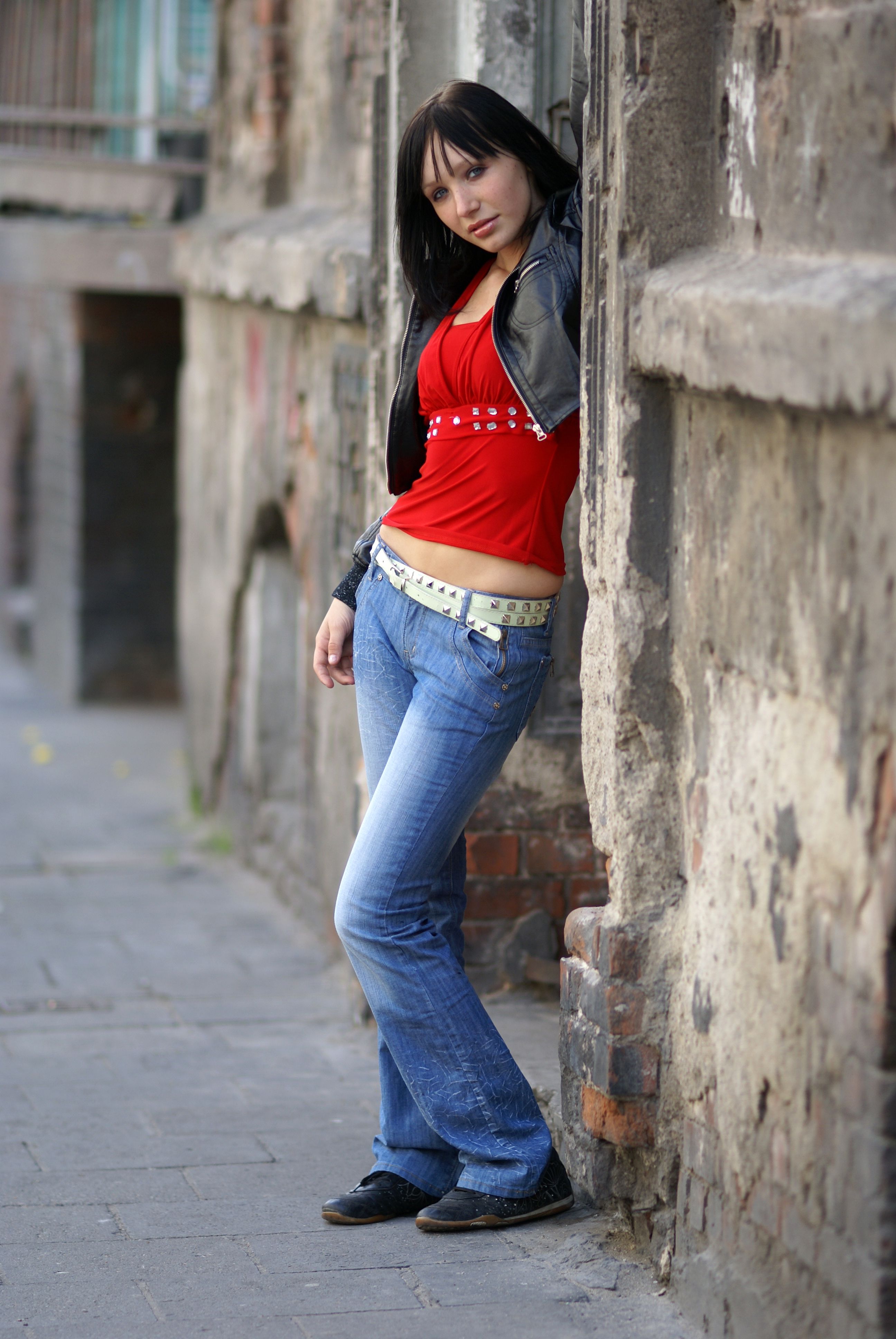 A woman leaning against a brick wall wearing a red shirt and jeans ...