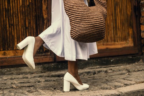 歩道を歩きながら白いドレスと白いハイヒールの靴を履いている女性