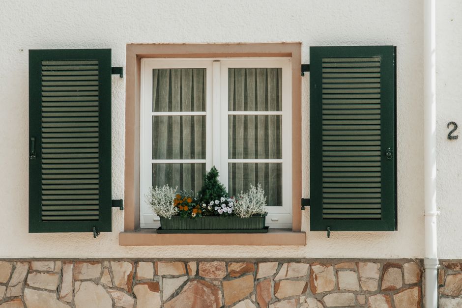 Elegant house exterior featuring green shutters, a white window, and a flower-filled planter.