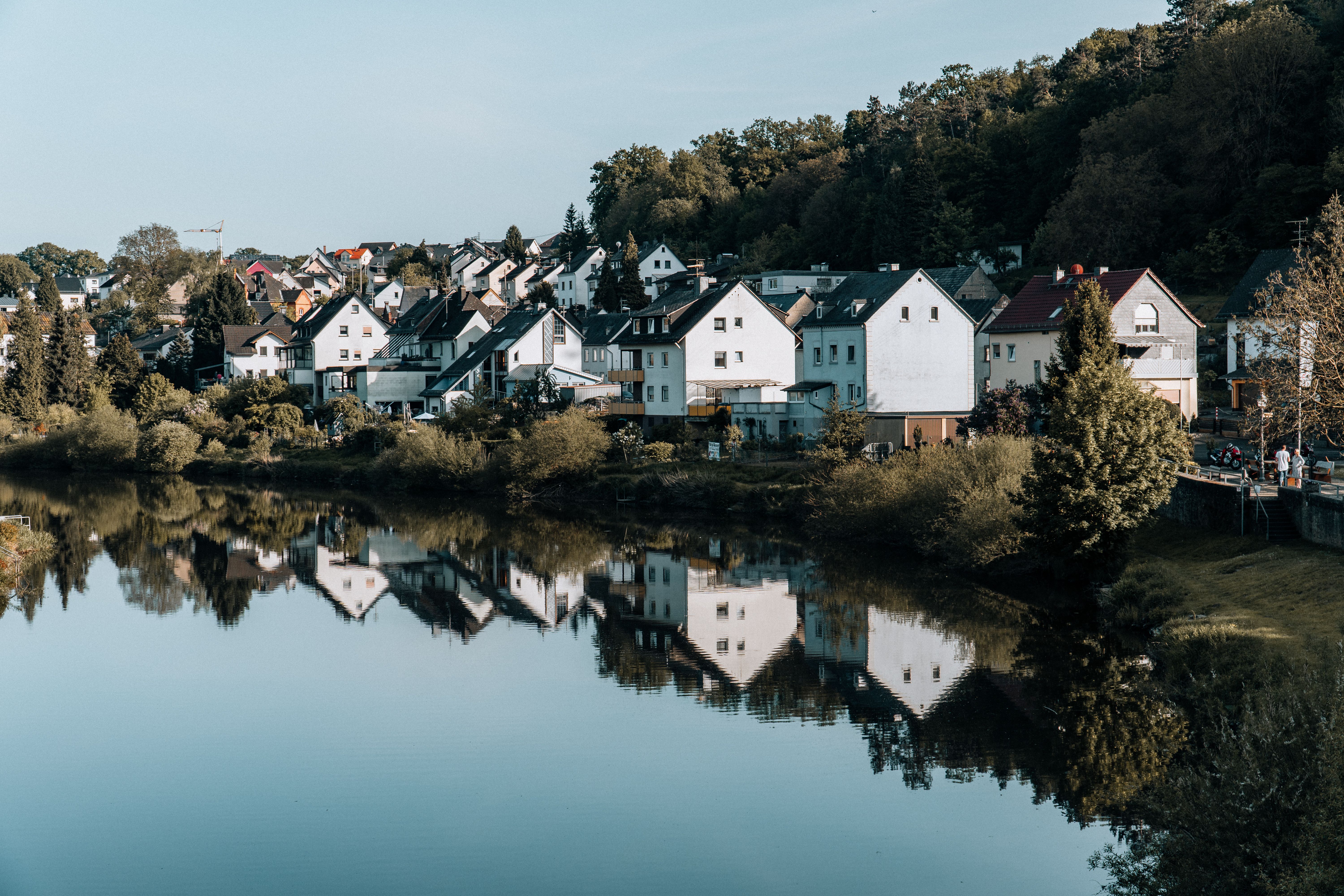 A picturesque view of a serene town by the river, reflecting charming houses and lush greenery.
