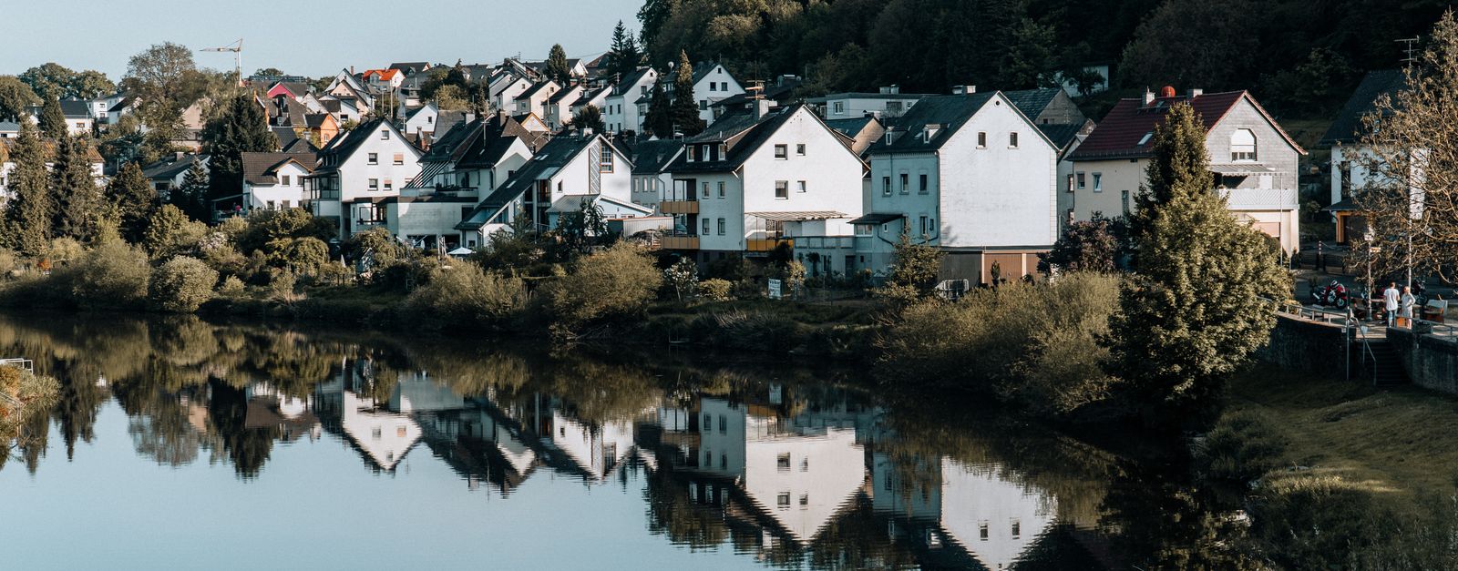 A picturesque view of a serene town by the river, reflecting charming houses and lush greenery.