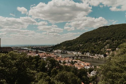 Free Idyllic landscape of Heidelberg with arch bridge, riverside town, and lush hills under a summer sky. Stock Photo