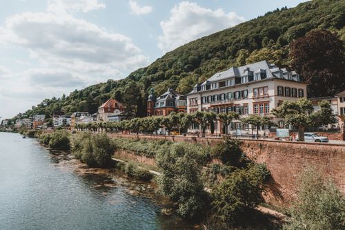 Free Picturesque riverfront architecture in Heidelberg, Germany with lush greenery and a serene atmosphere. Stock Photo