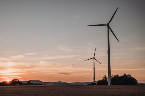 Free Wind turbines standing tall in a field against a serene sunset sky. Sustainable energy in harmony with nature. Stock Photo