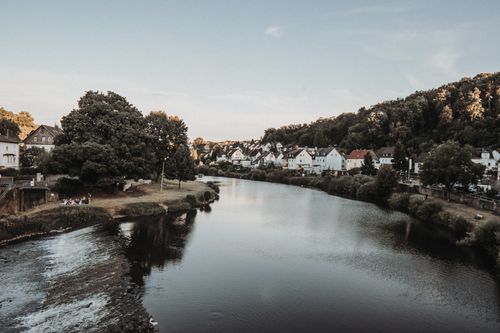 Free Charming European town by a serene river surrounded by lush hills and trees. Stock Photo