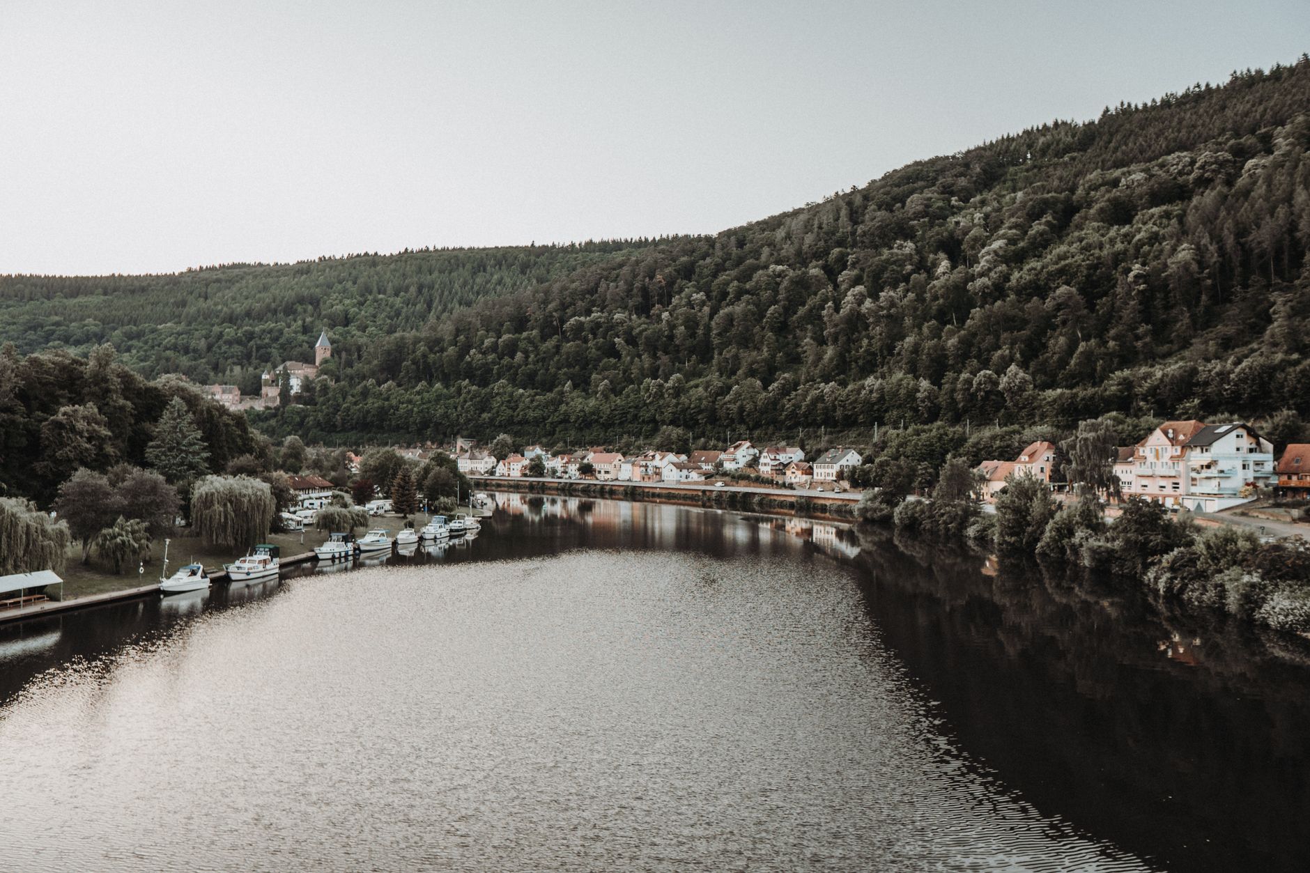 A picturesque view of a riverside town by a serene lake surrounded by verdant forests.