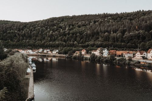 Free A peaceful riverside town set against lush, forested hills under a bright sky. Stock Photo