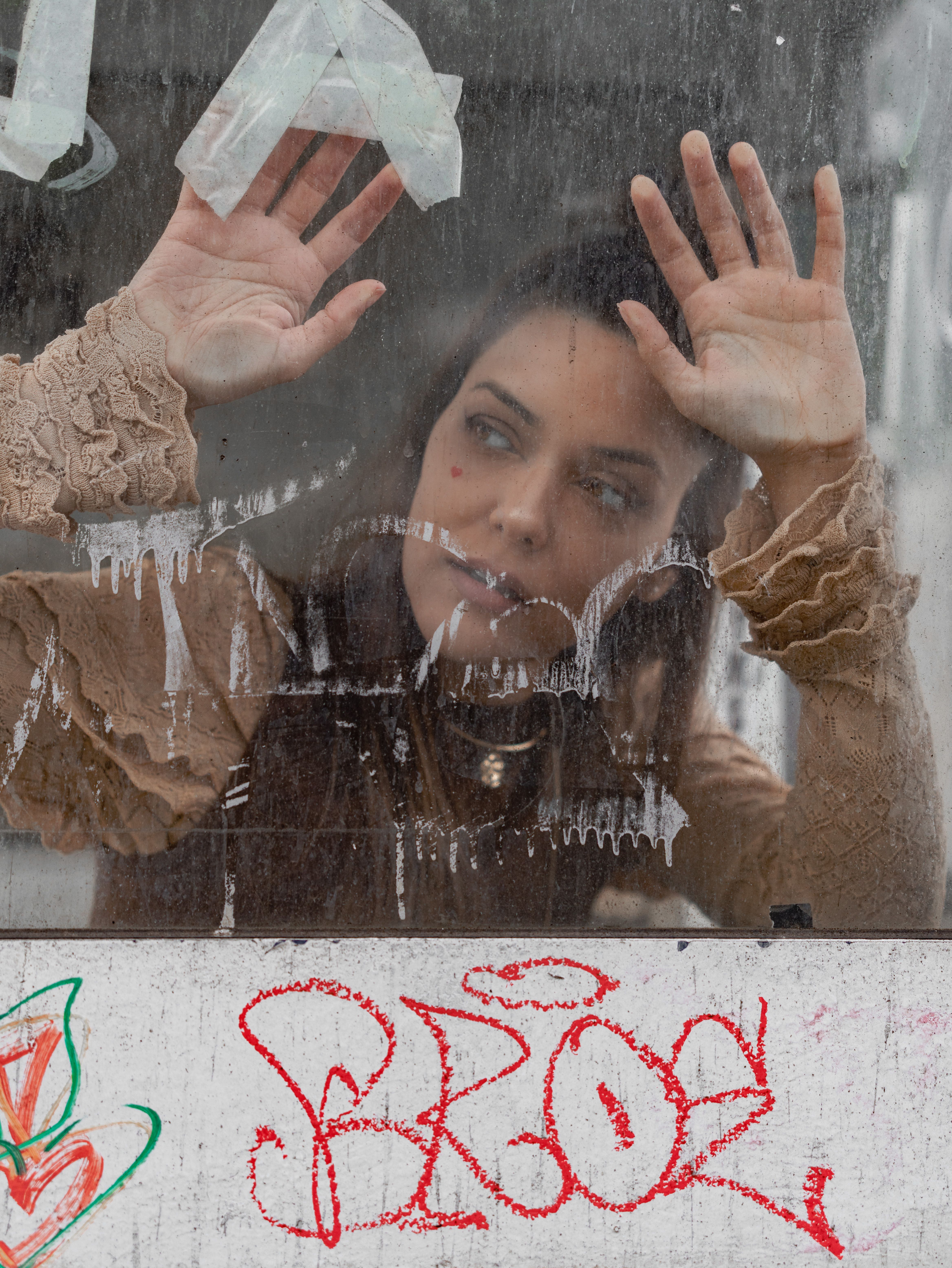 A contemplative woman looks through a dirty, graffiti-covered glass panel in Lisbon.