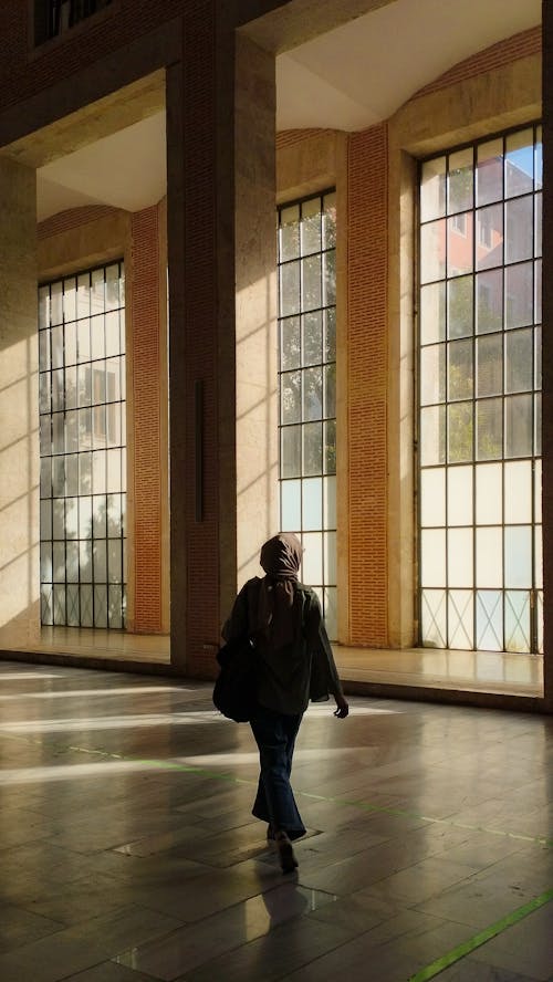 Back View of a Woman Walking in a Room with Large Windows 