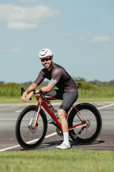 A cyclist in modern gear poses with his red bike on an open road under a clear sky.