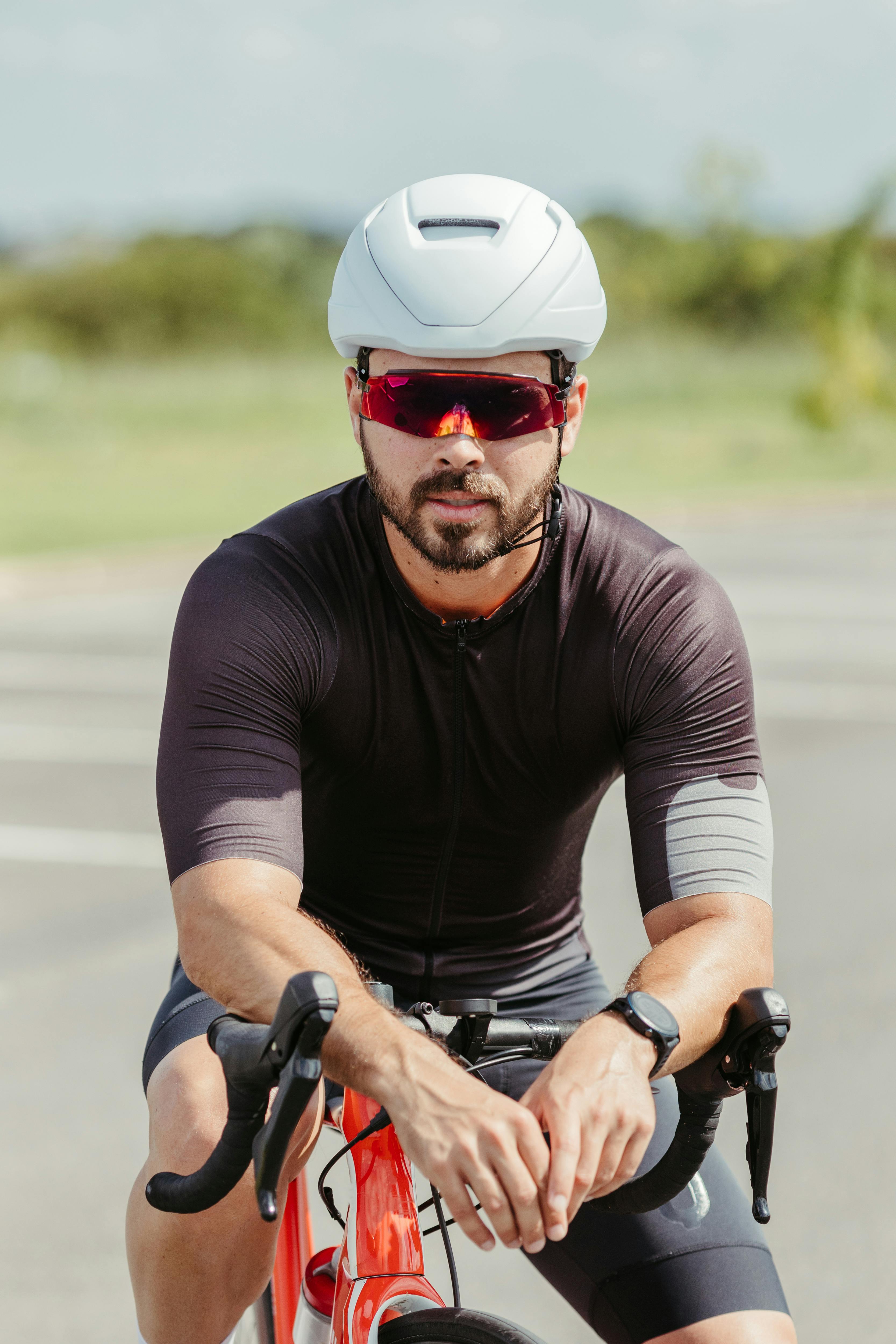 A man wearing a helmet and sunglasses rides his bicycle outdoors on a sunny day, embodying fitness and health.
