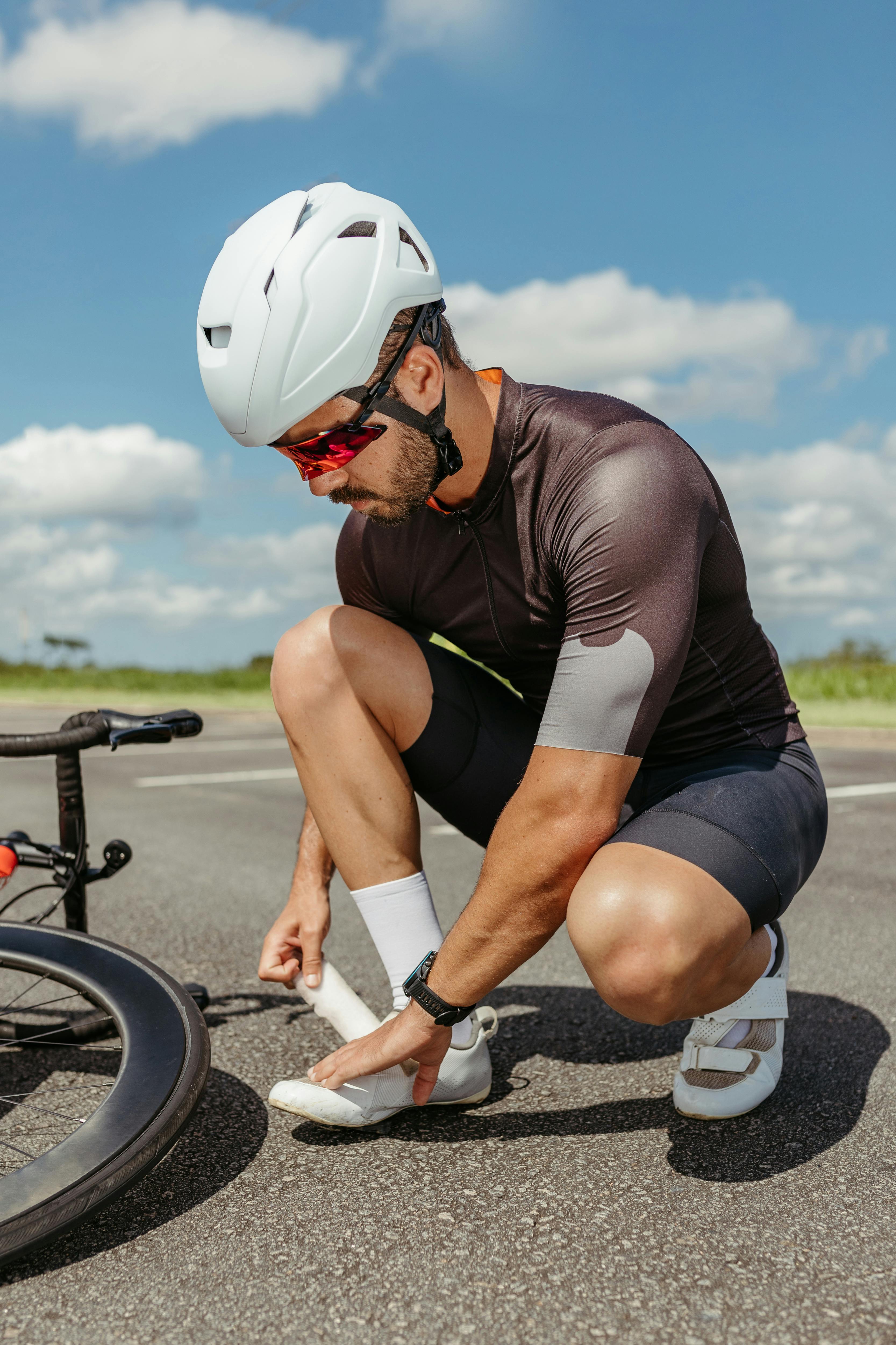A cyclist kneels to adjust his shoe on a sunny day, embodying fitness and outdoor activity.