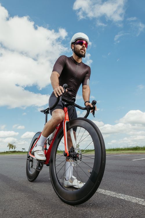 Free A male cyclist riding a bicycle on an open road under a clear sky. Stock Photo