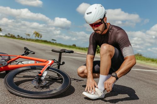Free Cyclist fixing shoes next to bike under clear sky, highlighting fitness and outdoor activity. Stock Photo