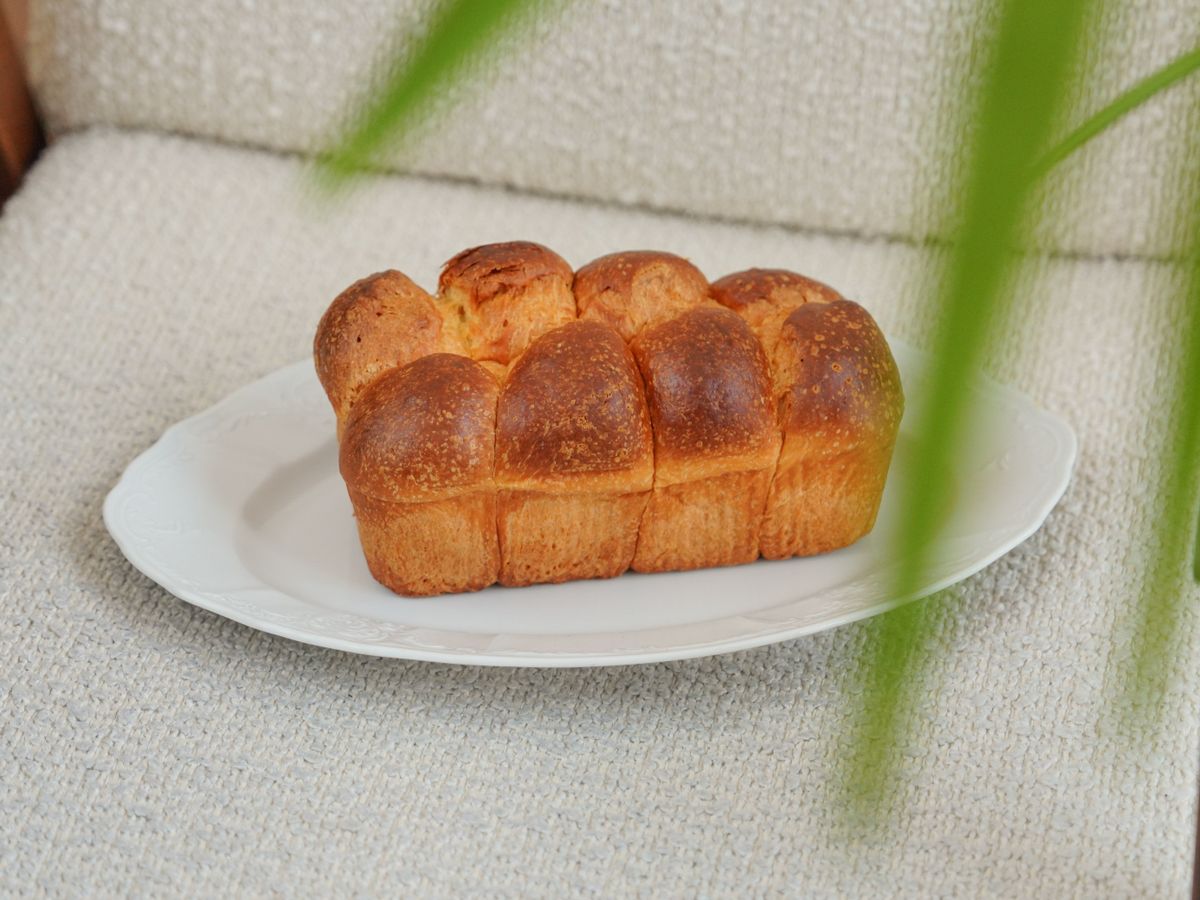 Shiny golden brioche loaf with rounded pull-apart sections resting on a white oval plate