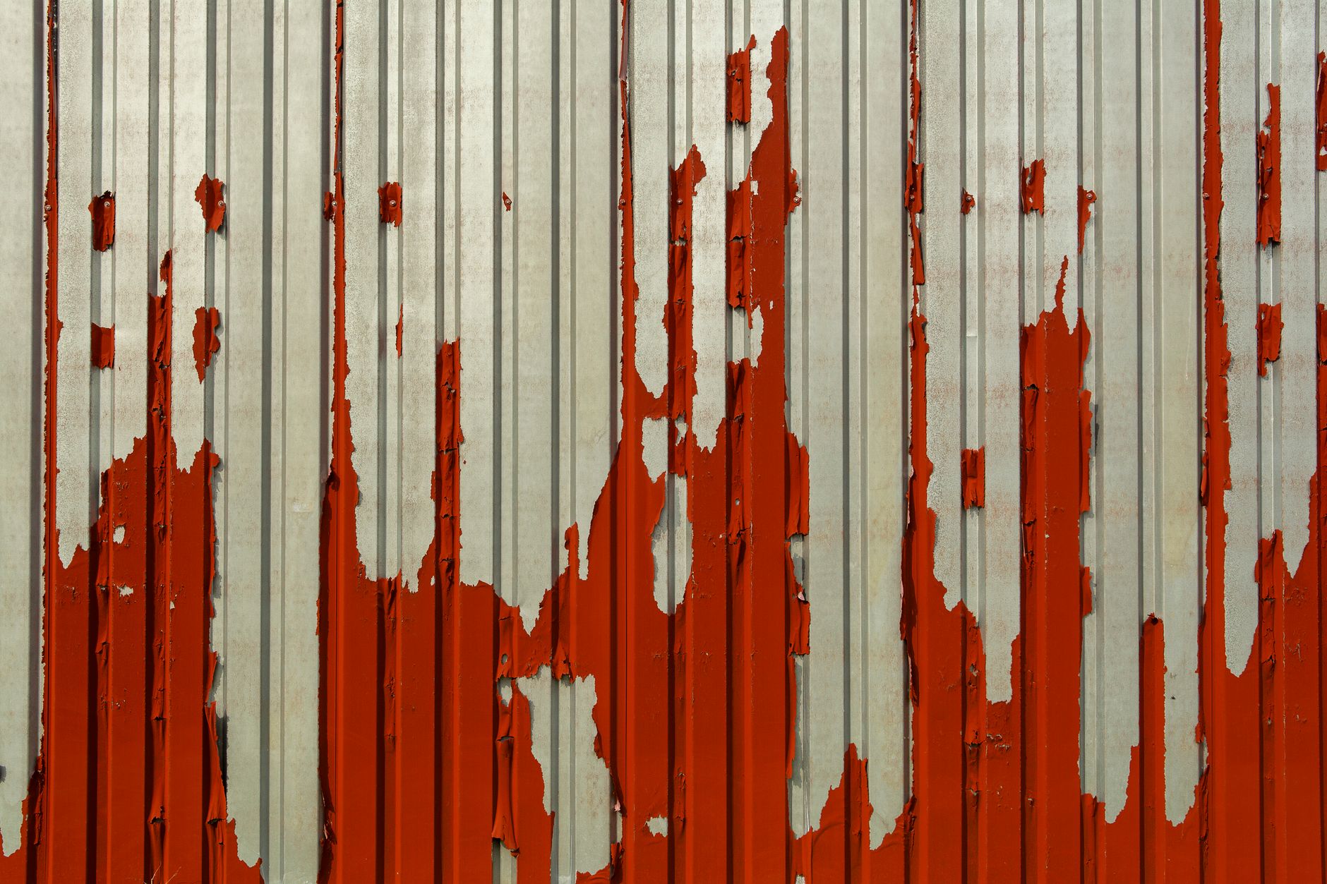 Close-up of a corrugated metal wall with red paint peeling off, showcasing aging and deterioration.
