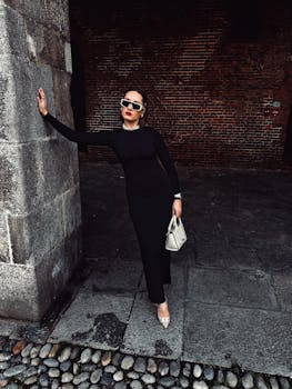 Stylish woman in black dress and sunglasses poses confidently in an urban setting.