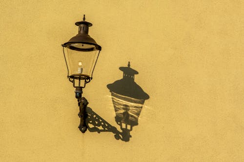 Free Old-Fashioned Street Light Casting Shadow on a Yellow Wall Stock Photo